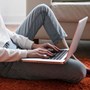 A woman sat down on the floor while working on a laptop.