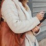 A lady leaning against a wall while using her phone.