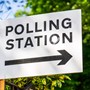 Photograph of a sign that says 'polling station' with greenery in the background